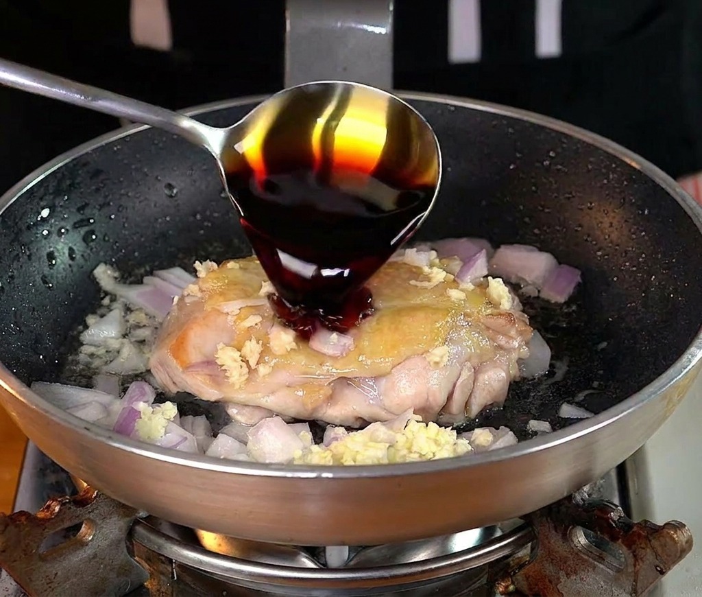 フライパンの中の鶏肉に薄口醤油を回しかけている様子