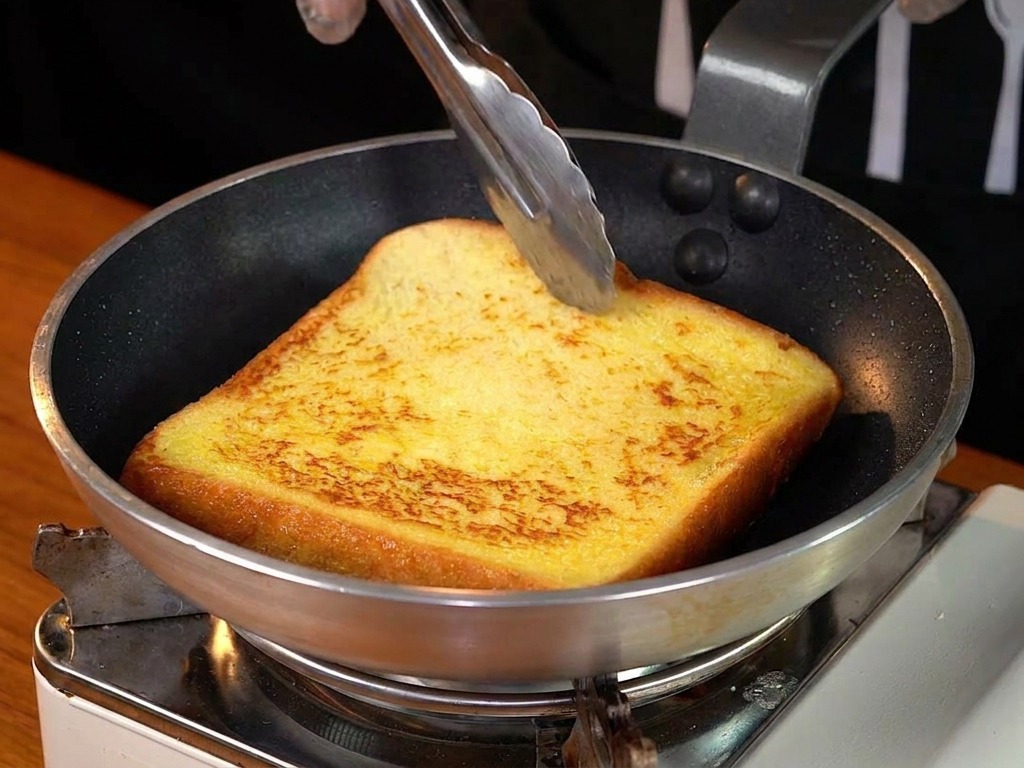 フライパンで黄金色に焼けたフレンチトーストを裏返している様子