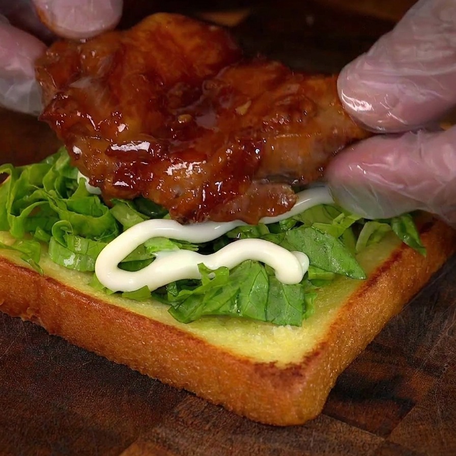 レタスをのせたパンの上に照り焼きチキンを配置している様子