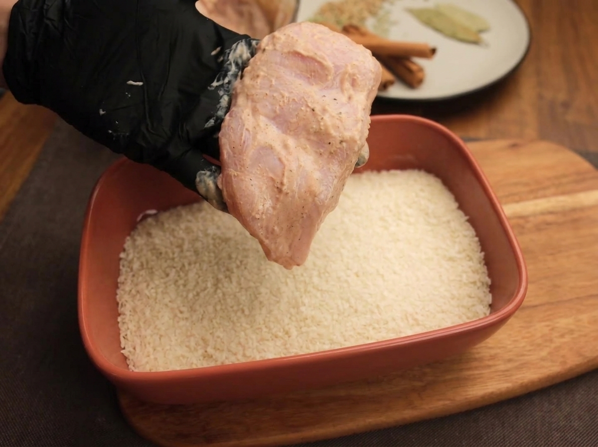 パン粉が入ったトレイの上で、マリネした鶏肉に衣をつけている様子。