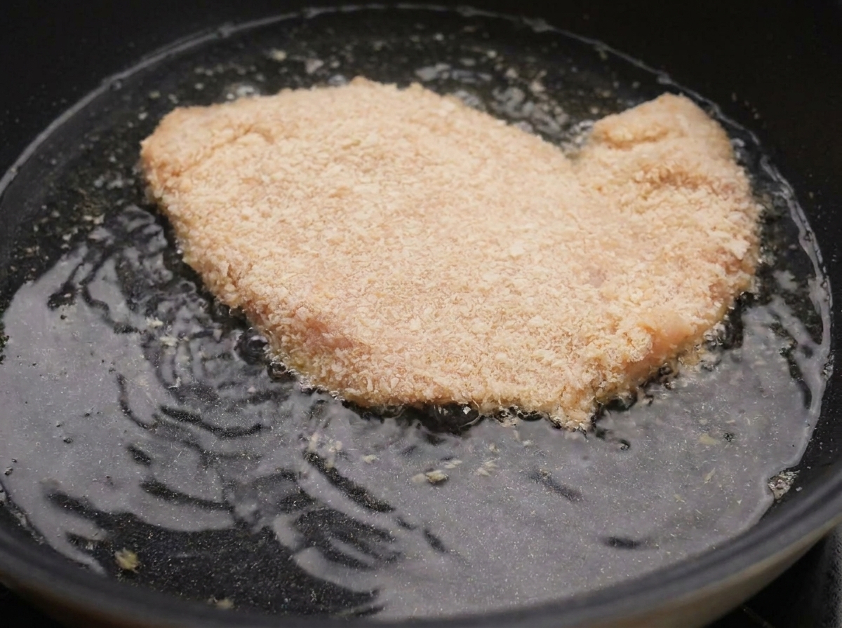 熱した油の入ったフライパンで、衣をつけた鶏肉が泡を立てて揚がっている様子。