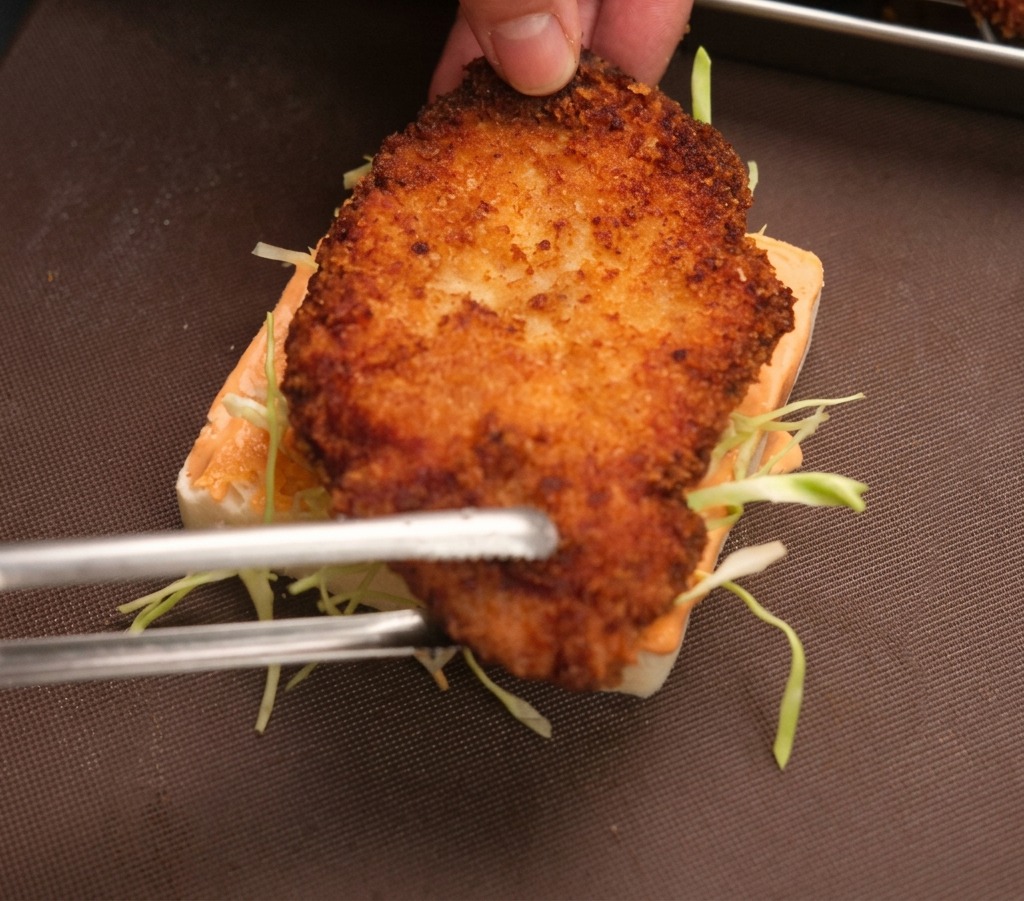 トングを使い、キャベツの上に揚げたてのチキンをのせている様子。