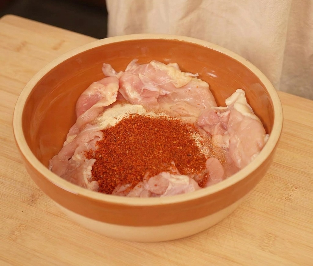 茶色のボウルに入った鶏肉に粉唐辛子などの調味料をまぶしている様子