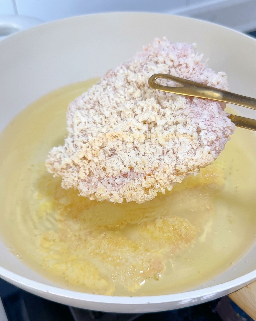 熱した油に冷凍の鶏カツをトングで静かに入れている様子。