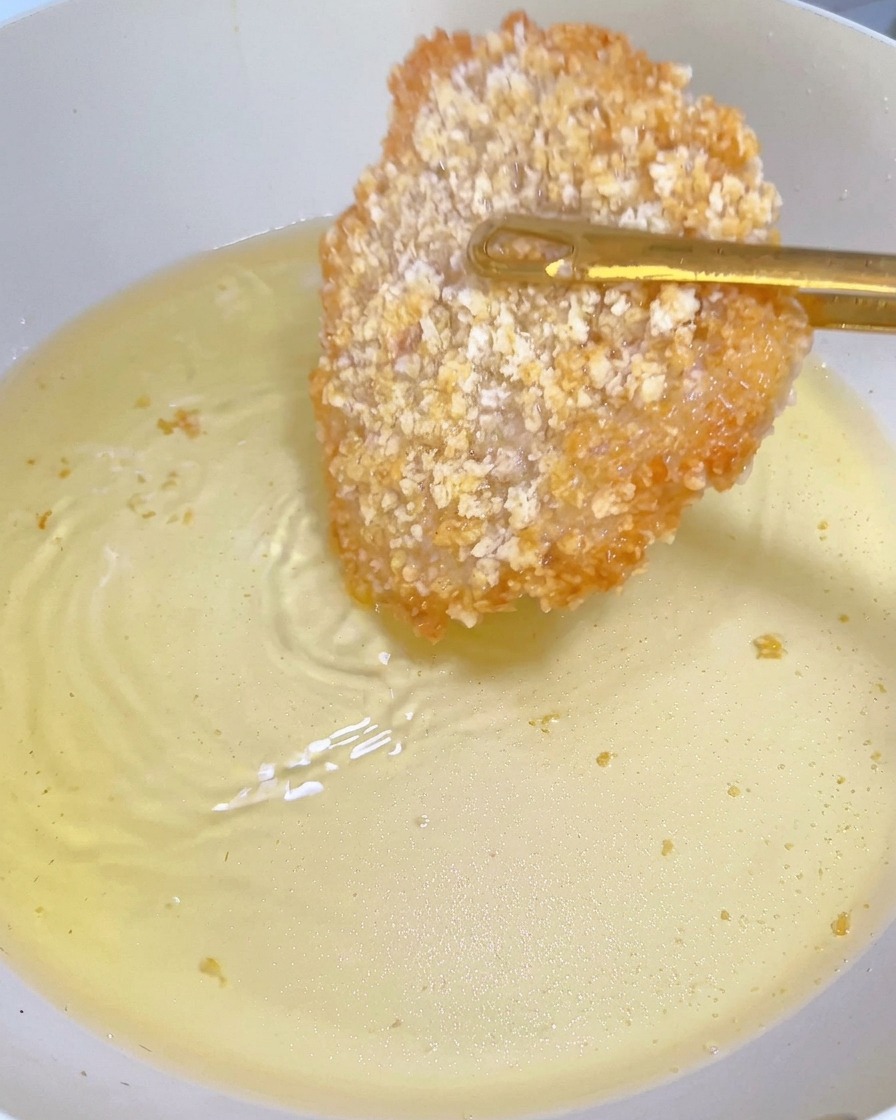きつね色に色づいた鶏カツをトングで裏返している様子。
