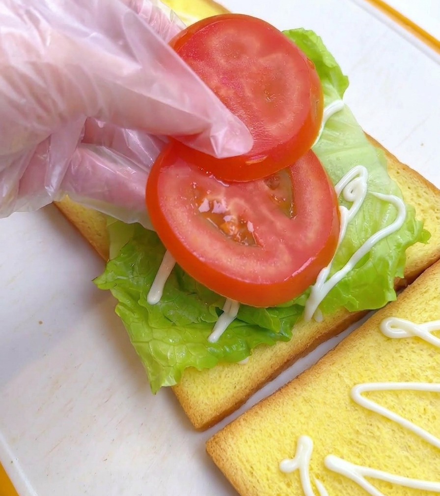 レタスの上にスライスしたトマトを2枚並べている様子。