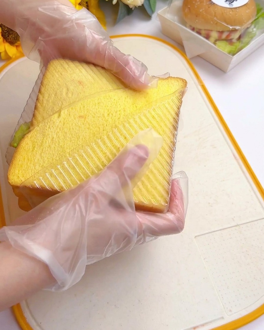 完成したサンドイッチを三角形の透明ケースに収めている様子。