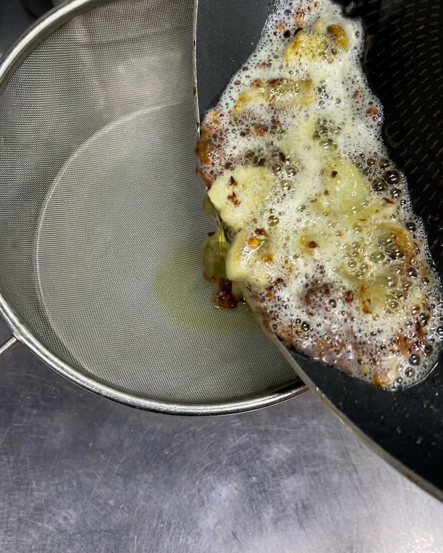 揚げたにんにくと油の混合物を、りんごのスライスを置いたザルで漉している様子。