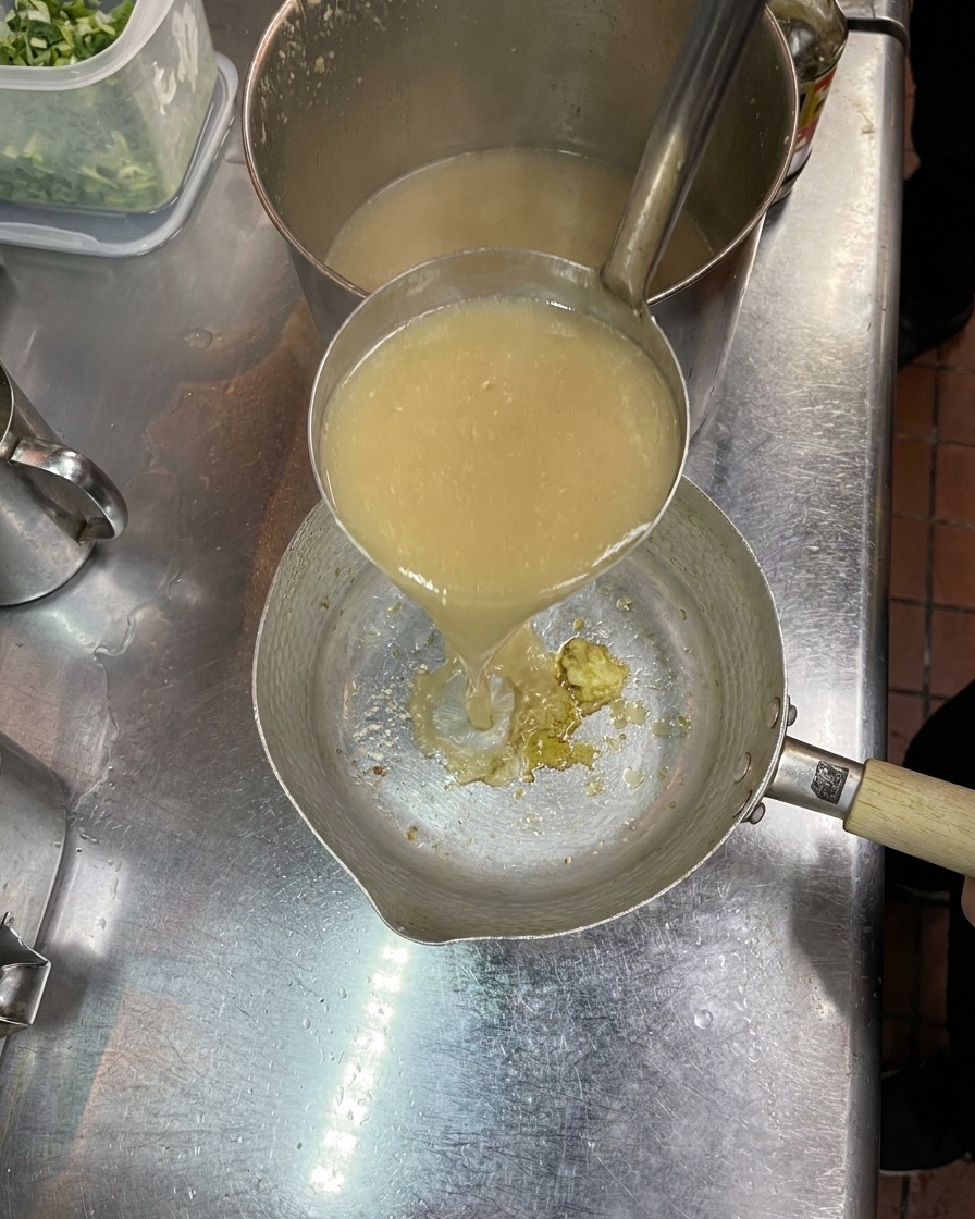 小さな鍋に入れた調味料に、お玉で熱々の豚骨スープを注いで混ぜている様子。