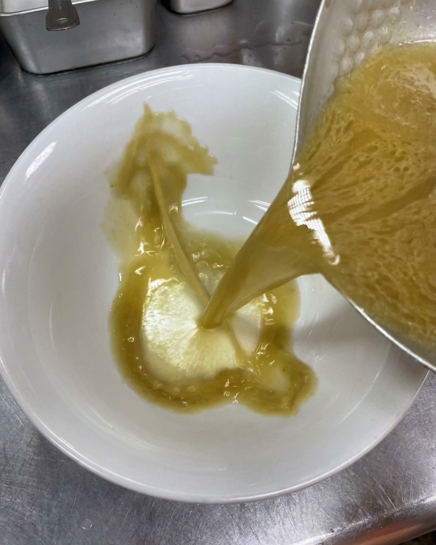 温めた陶器の丼に、味を整えた濃厚な豚骨スープを注いでいる様子。