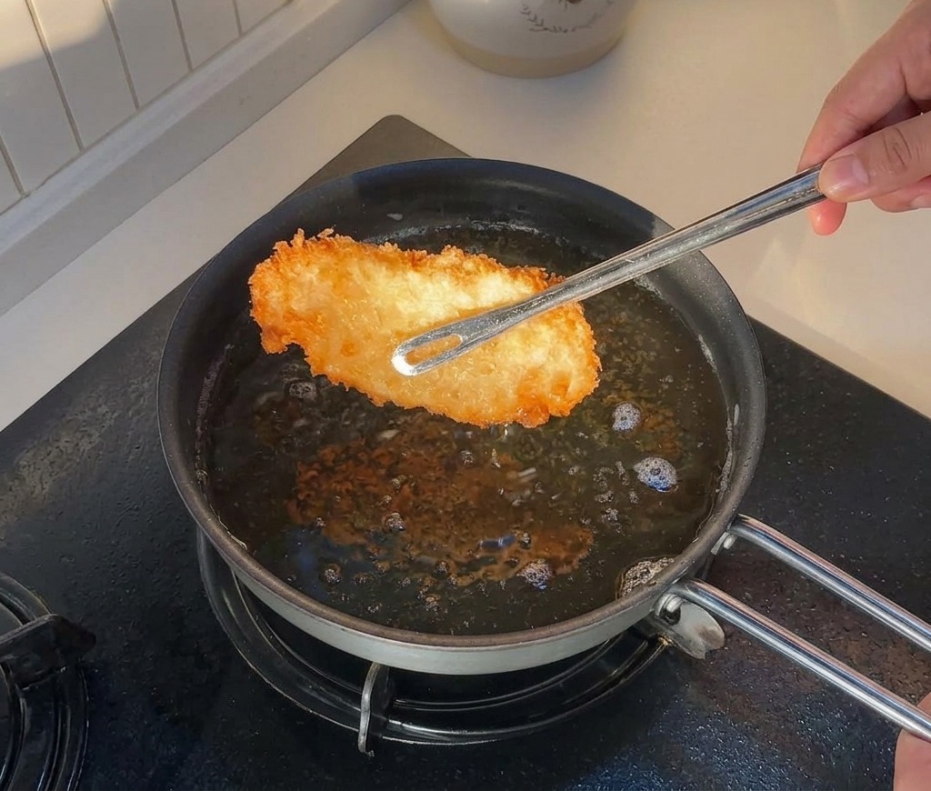 揚げ色のついた鶏肉をトングで油から持ち上げている様子。