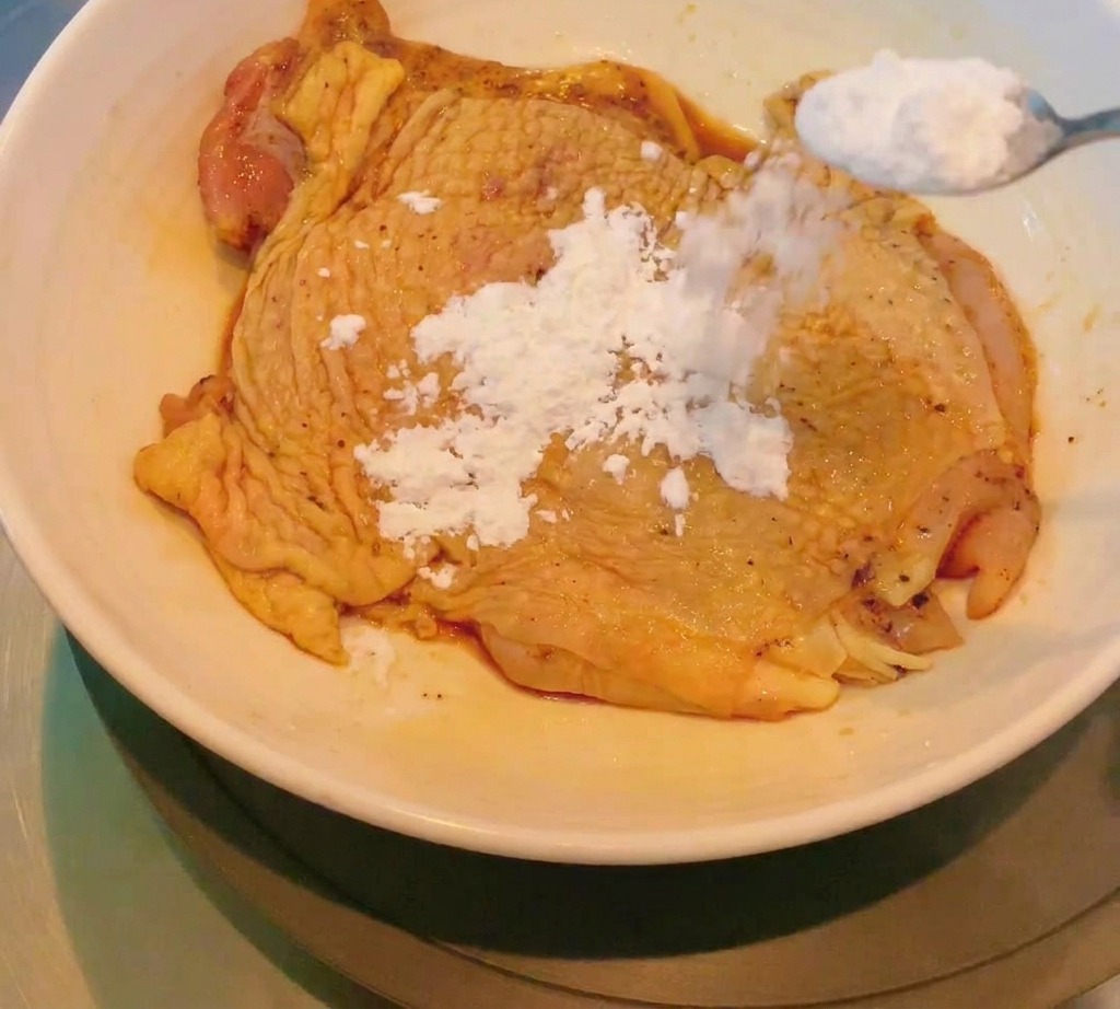 マリネされた鶏肉に、白い片栗粉をスプーンで振りかけて薄く均一な層を作っている様子。