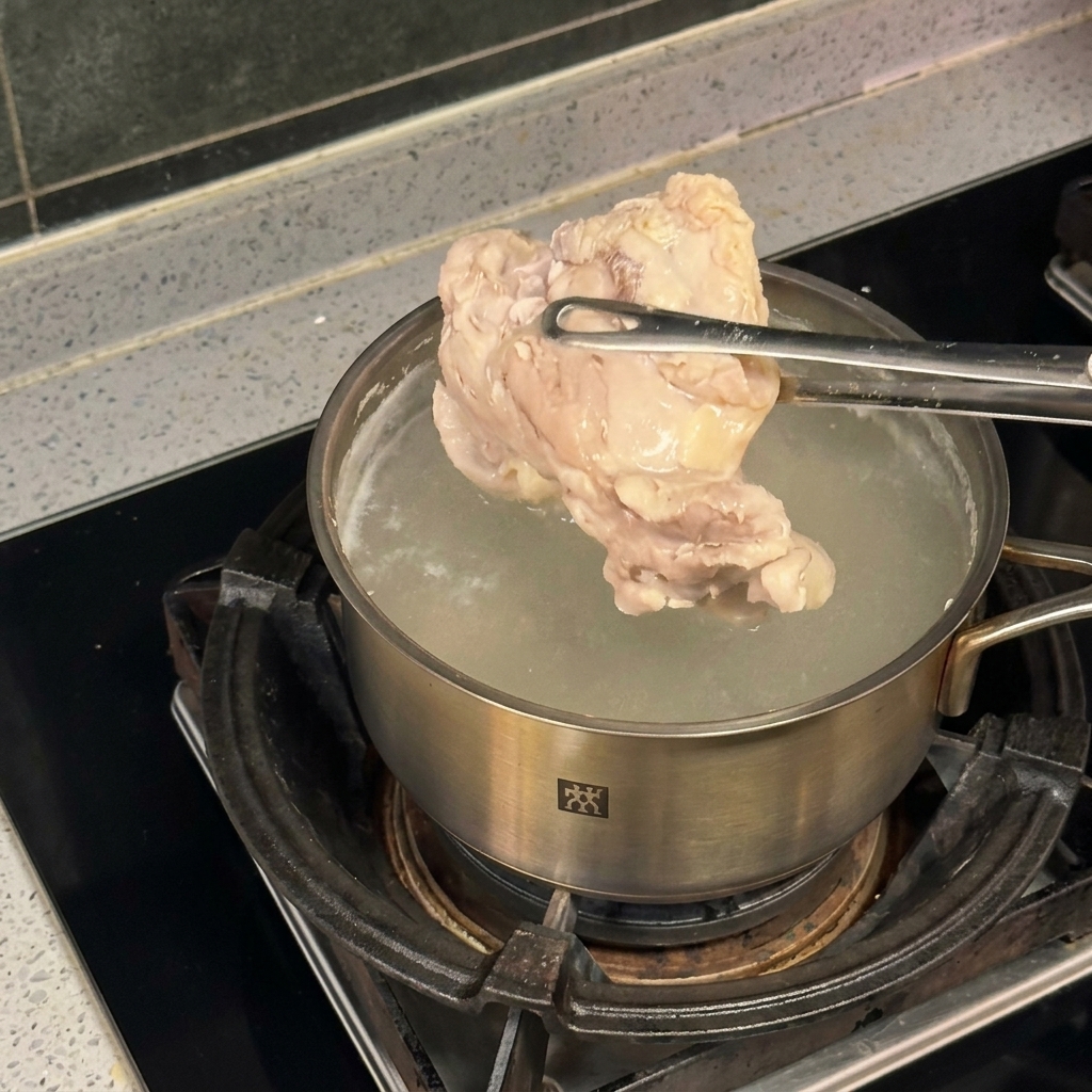 沸騰した鍋の上でトングを使い、鶏肉を茹でている様子。