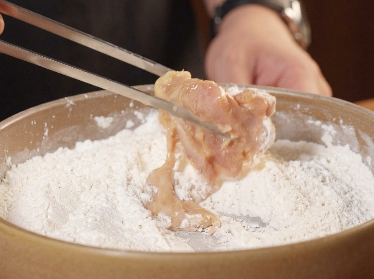 マリネした鶏肉を粉の中に投入し、手で押さえるようにして衣をつけている様子。