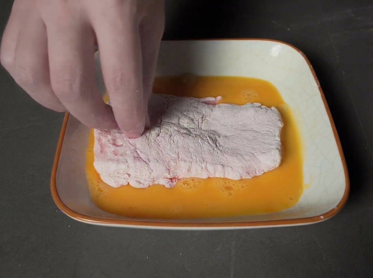 卵液を通した肉をパン粉の上に置き、手でしっかり押さえる様子。