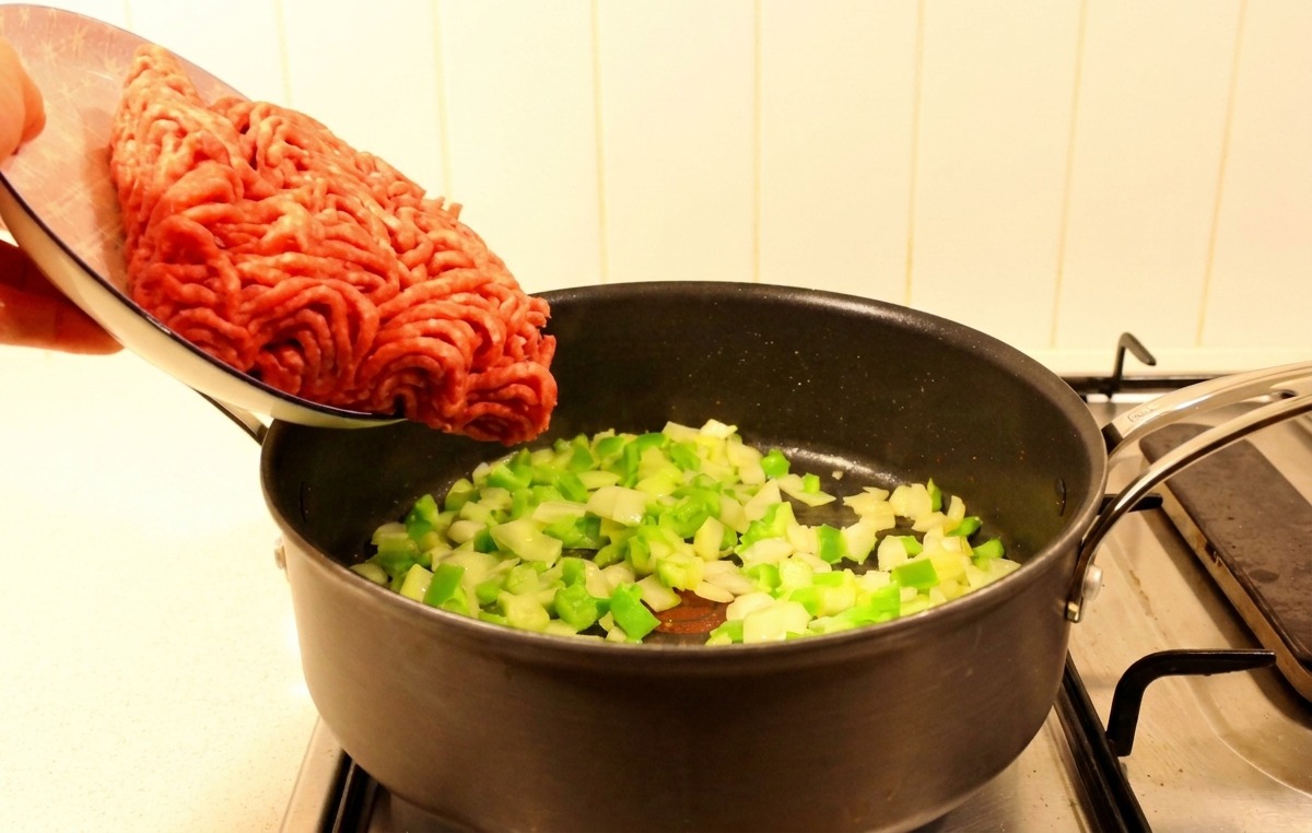 炒めた野菜が入ったフライパンに生の牛ひき肉を投入する様子。