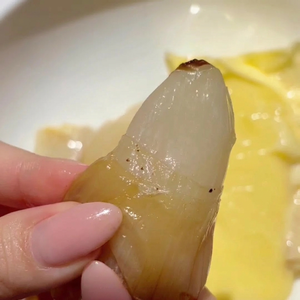 薄皮から黄金色に透き通ったローストにんにくの身を、手で押し出している様子。
