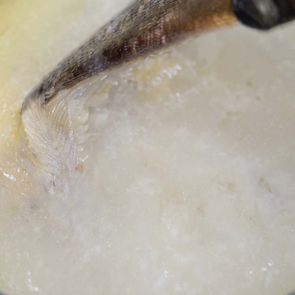 フライパンのルーに風味付けした牛乳を注ぎ入れ、木べらで混ぜ合わせている様子