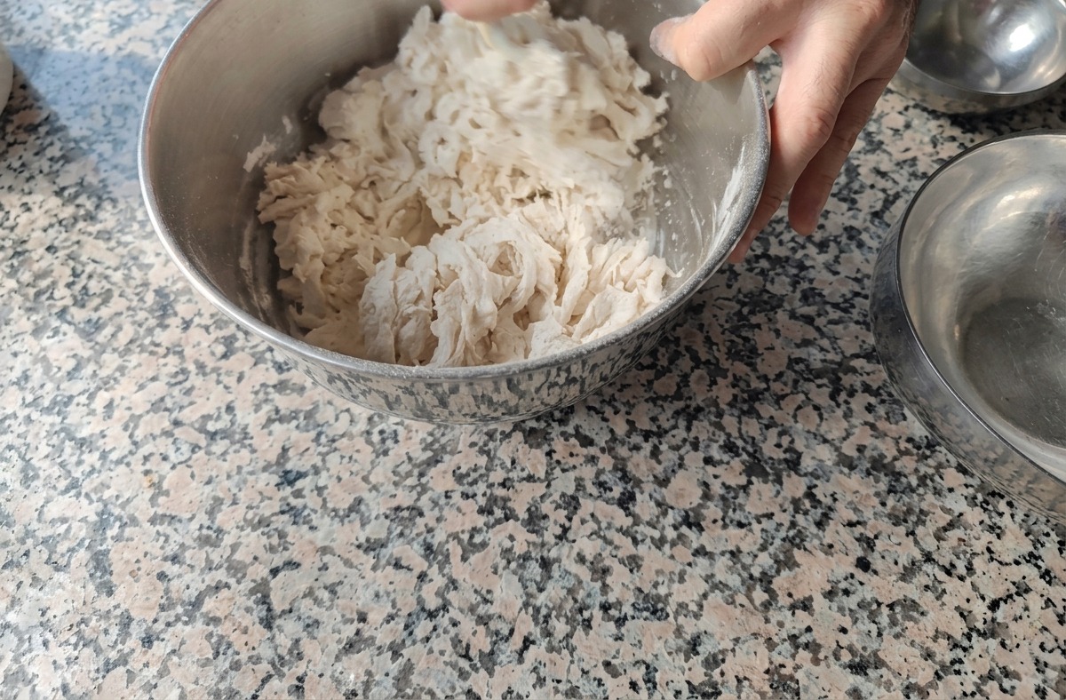 金属製のボウルの中で、手を使って小麦粉と水を混ぜ合わせ、ゴツゴツとしたまとまりのないビガ種を作っている様子。