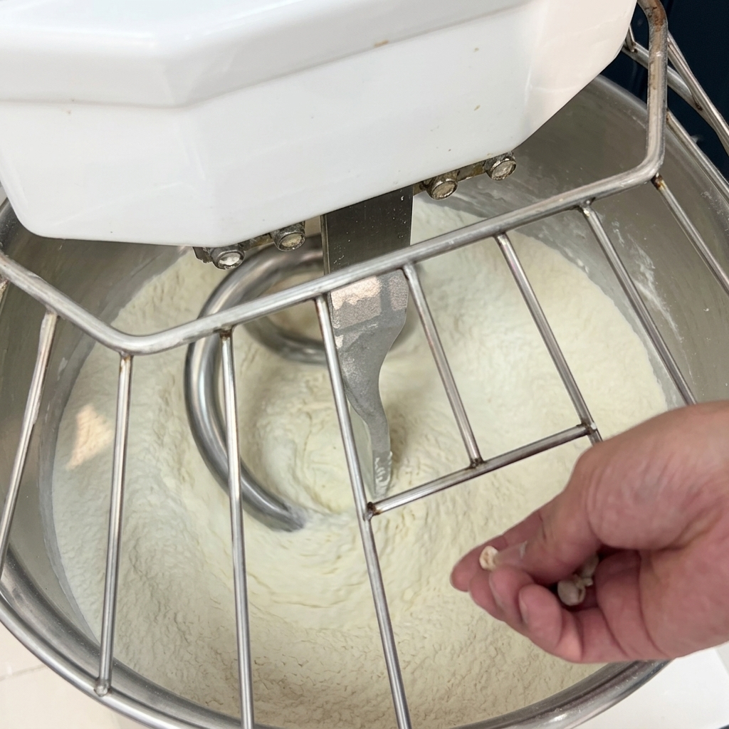 稼働中のスパイラルミキサーの中にある小麦粉に、手で細かく崩した生イーストを加えている様子。