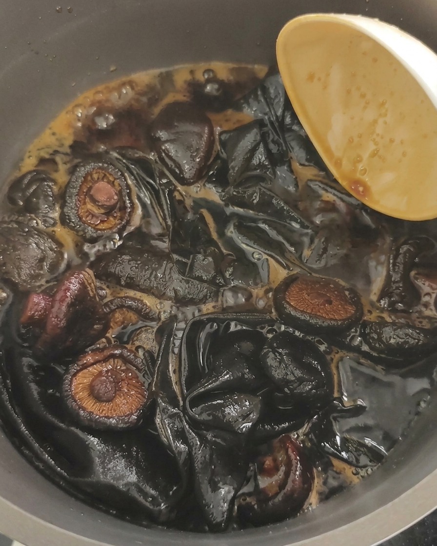 醤油ベースの黒い煮汁で、きくらげと大きめの昆布を煮込んでいる様子