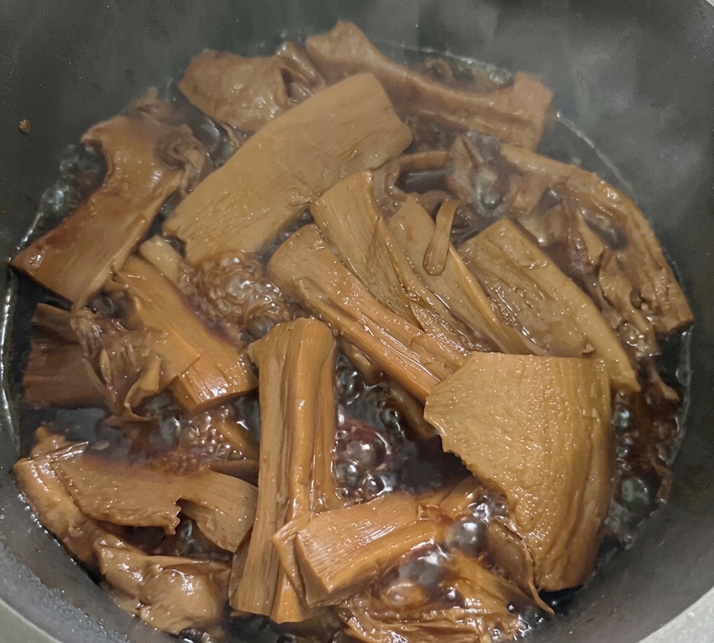 鍋の中で醤油ベースのタレと共に煮込まれているスライスされたメンマ
