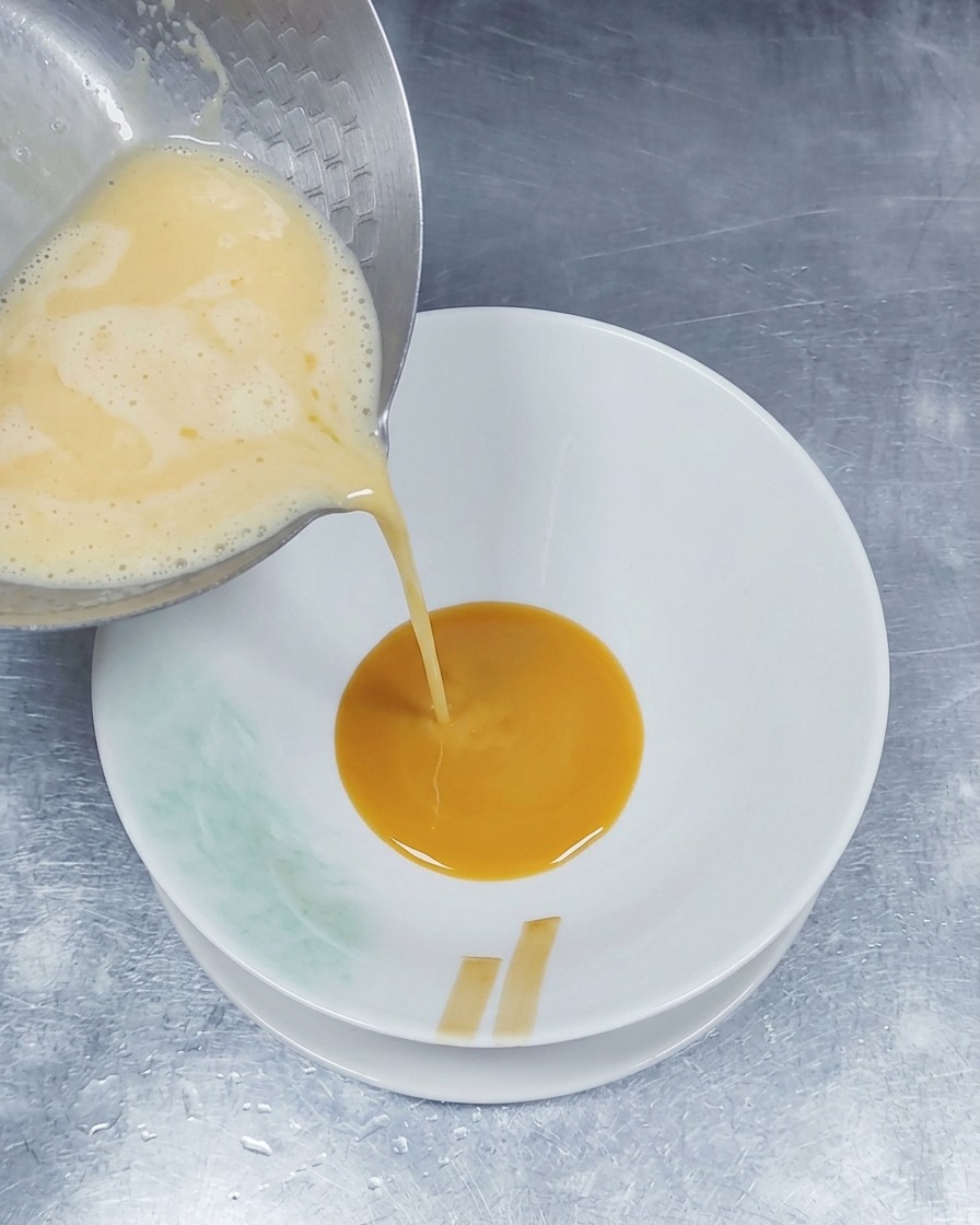茶色いタレが入った丼に、鍋から熱々で少し泡立つ白い豚骨スープを注いでいる様子