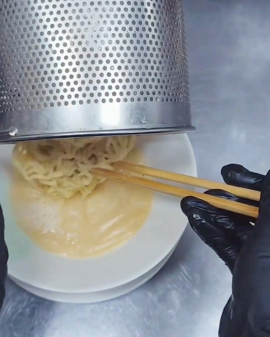 テボ(振りザル)から、濃厚な豚骨スープが張られた丼へと茹で上がったウェーブ麺を移している様子