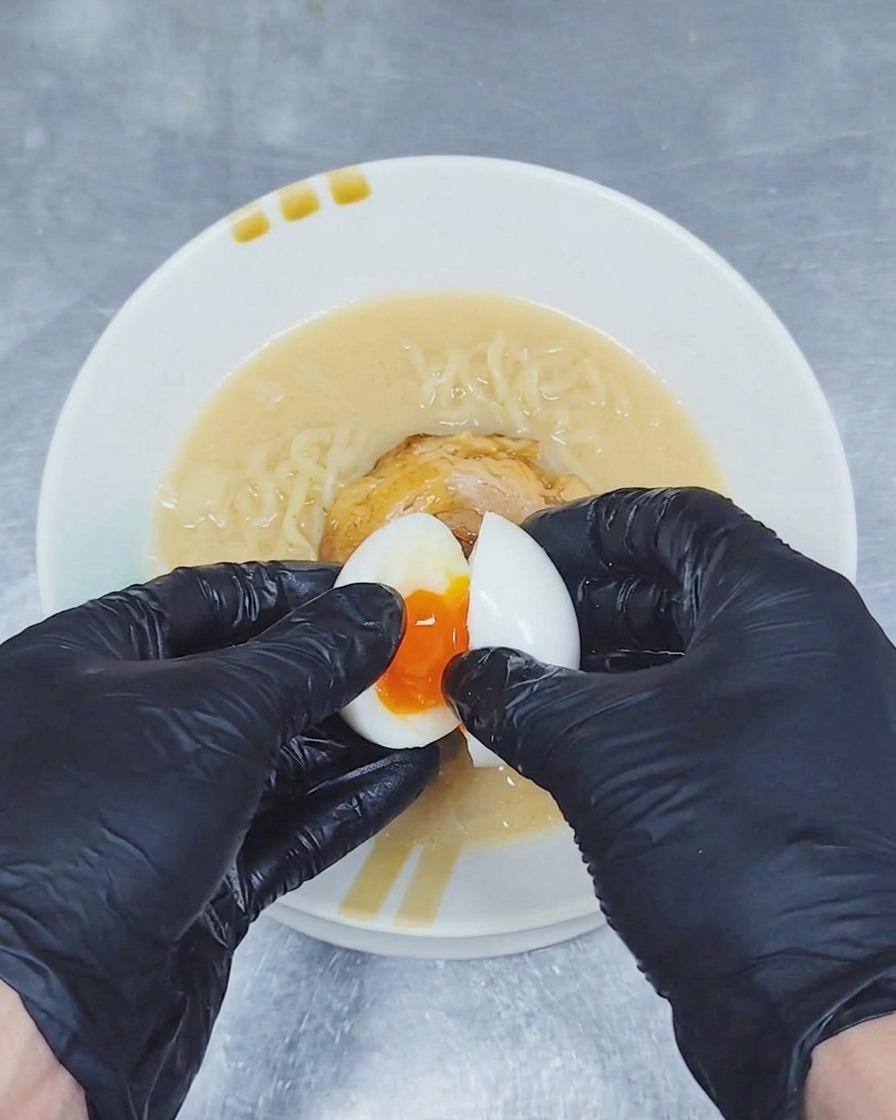 半分に割った味付け卵からとろりとした黄金色の黄身が覗く様子を、ラーメンの丼の上に盛り付けている手元
