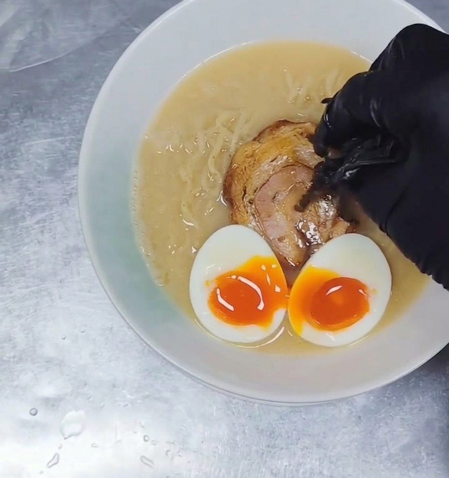 チャーシューや卵がのったラーメンの器に、細切りの黒いキクラゲをひとつまみ添えている様子