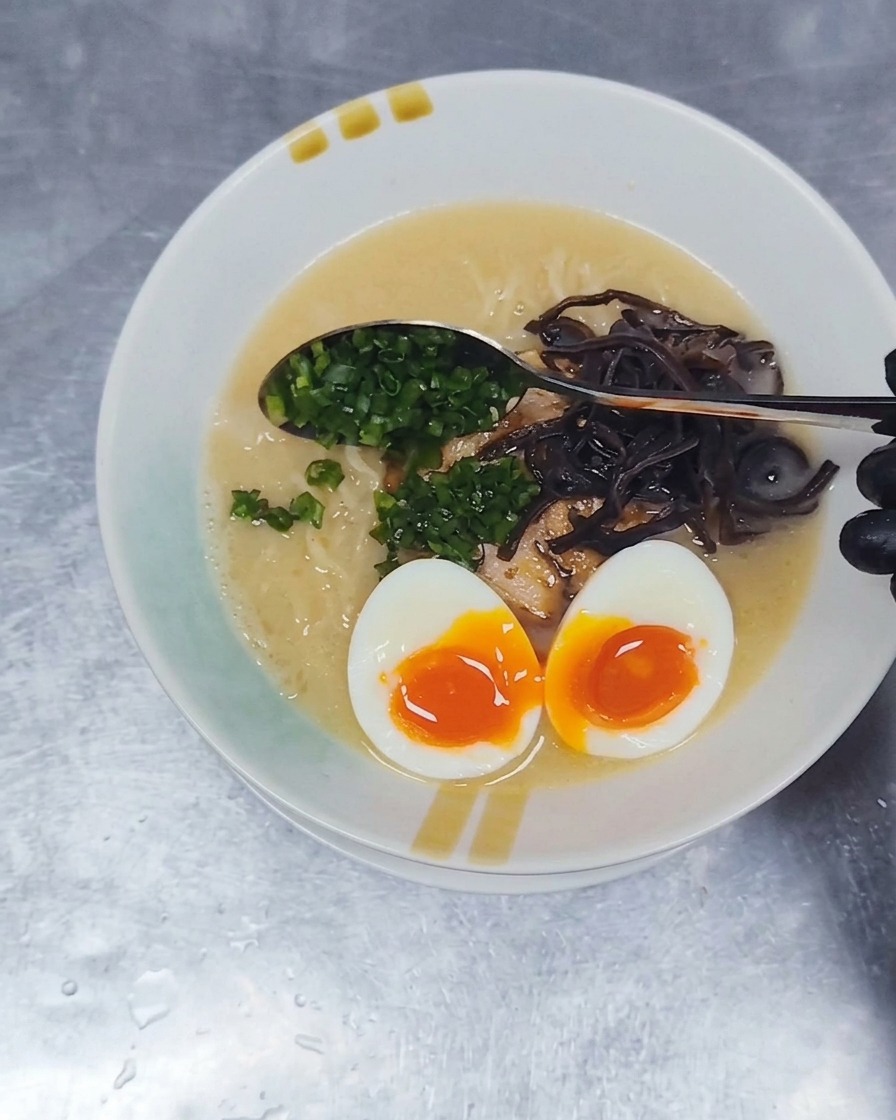 スプーンを使い、盛り付けられた豚骨ラーメンの中央に細かく刻んだ青ネギを散らしている様子