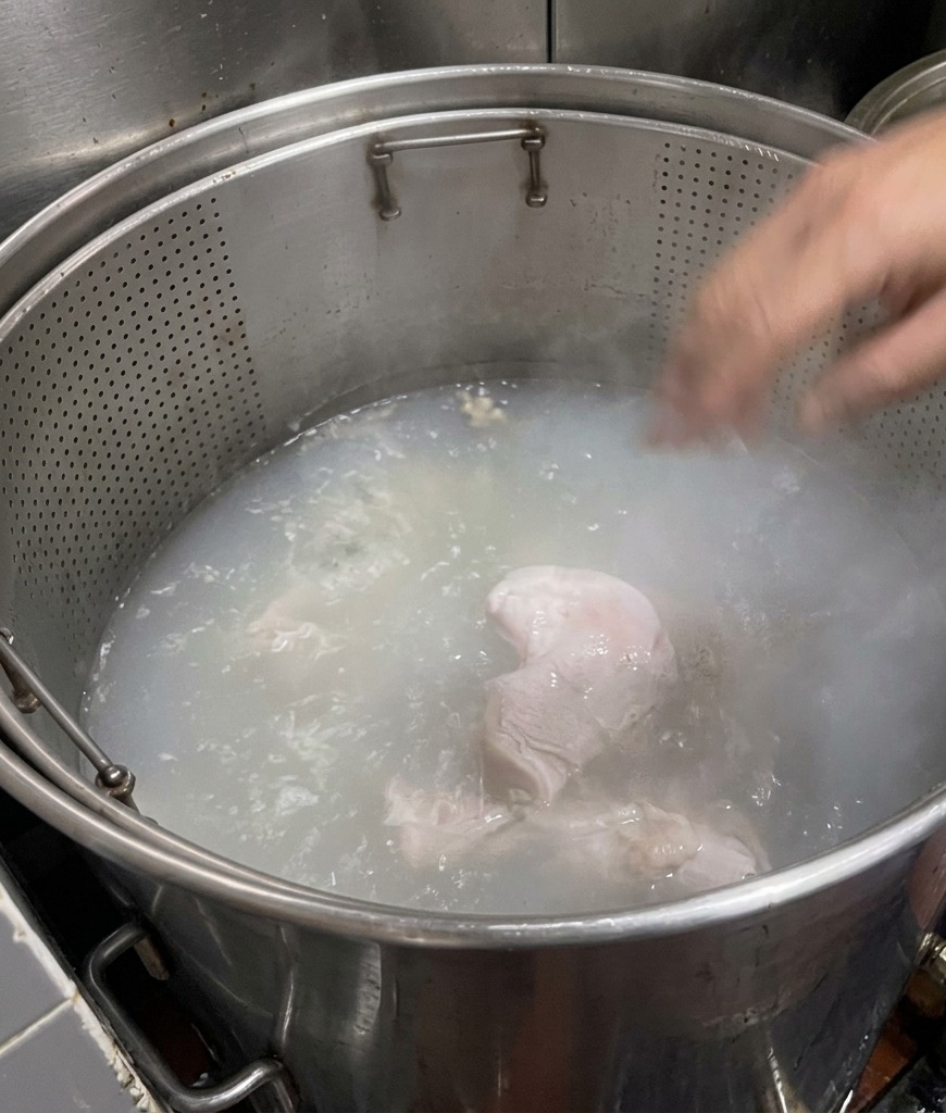 大きな鍋の中で沸騰するお湯に浸かった豚骨。透明だったお湯が、徐々に白濁したミルク色へと変化している様子。
