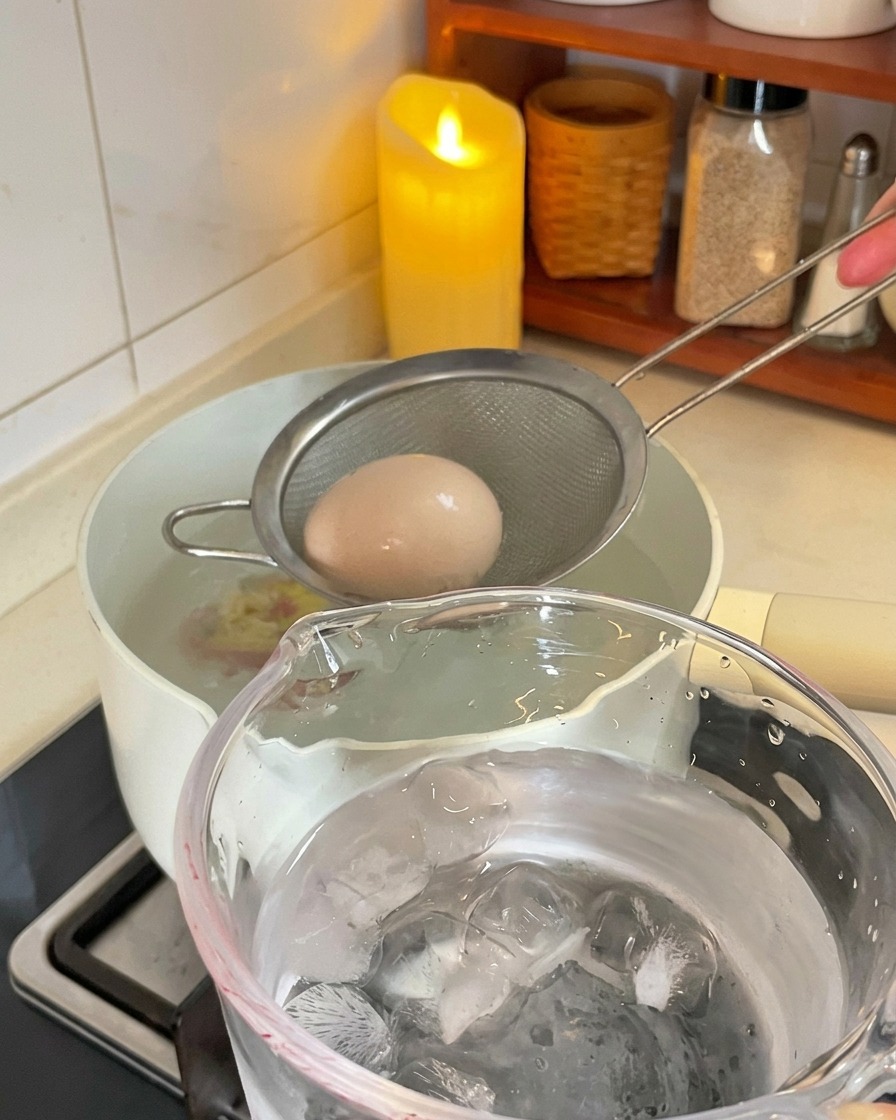 茹で上がり卵を鍋からすくい上げ、氷水の入った容器に移す様子