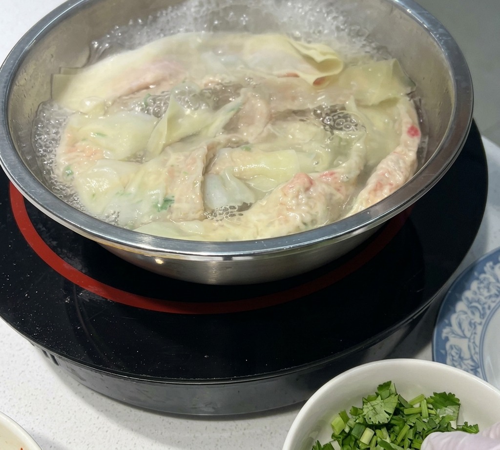 ステンレス製の鍋に沸騰したお湯の中で茹でられている手延べワンタン麺。いくつかの麺が表面に浮き上がっている。