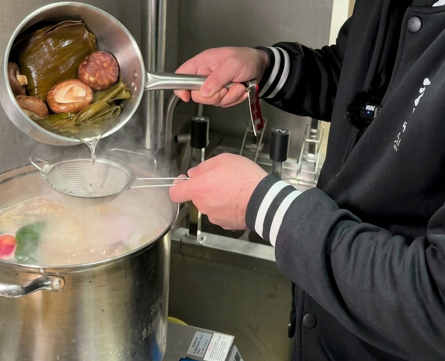 黄金色に輝く椎茸と昆布の出汁を、細かいザルを通して沸騰した大きなスープの鍋に注ぎ入れている様子。