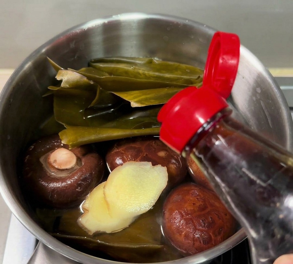 戻した椎茸、昆布、スライスした生姜が入った小さな片手鍋に、ボトルからナンプラーを注いでいる様子。