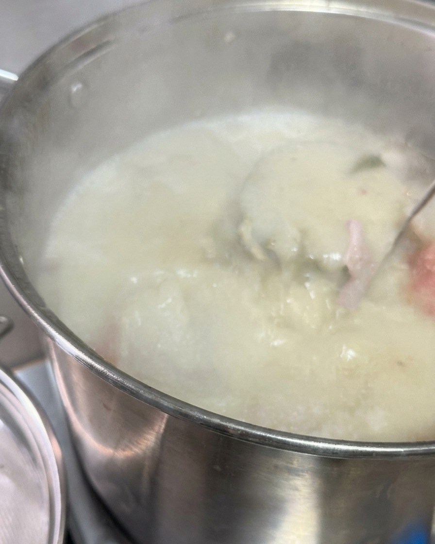 濃い調味タレとラードが入った小鍋に向かって、ザルを通して乳白色の豚骨スープを直接注ぎ入れている様子。