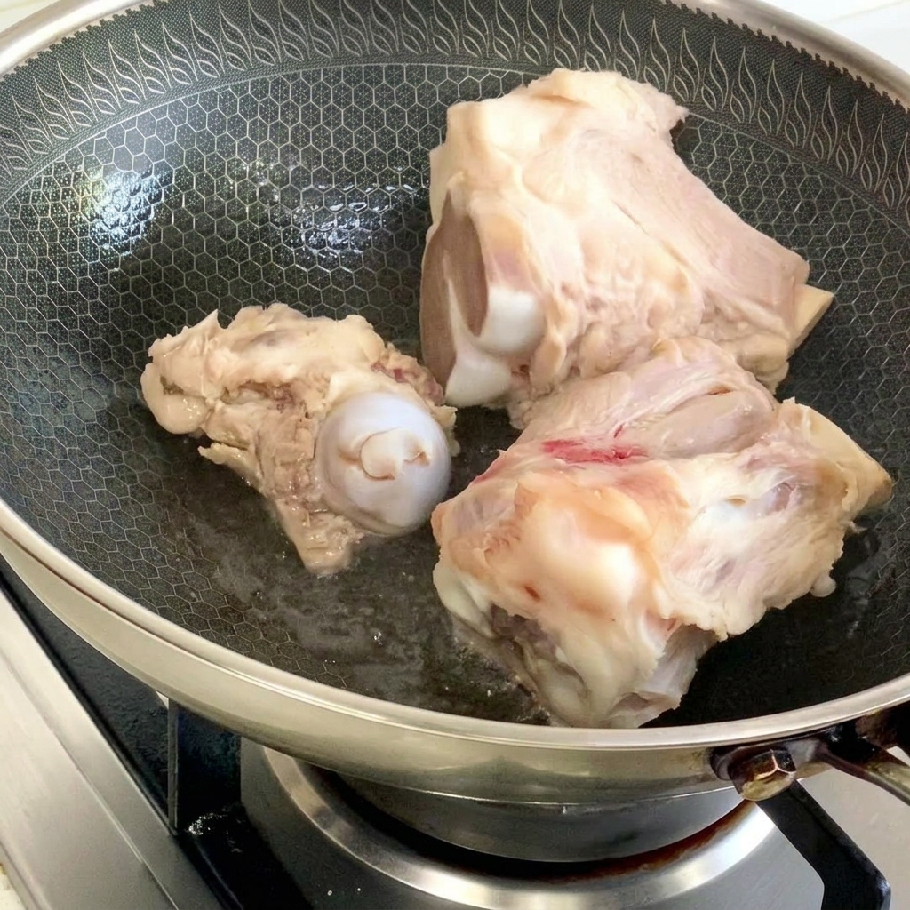 ハニカム模様の中華鍋に少量の油をひき、豚骨を香ばしく炒め焼きにしている様子。