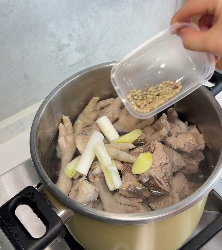 豚骨、鶏もみじ、長ねぎ、生姜が入った鍋にホワイトペッパーを加える様子。