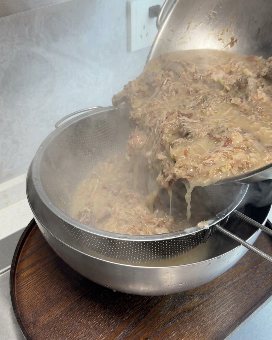 目の細かいザルを使って、濃厚な豚骨スープからお肉の端材を濾し取る様子。