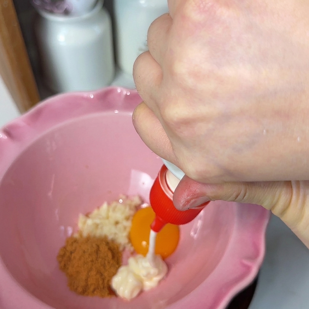 どんぶりの中に、おろしにんにく、卵黄、粉末スープを入れ、マヨネーズを絞り入れる様子。