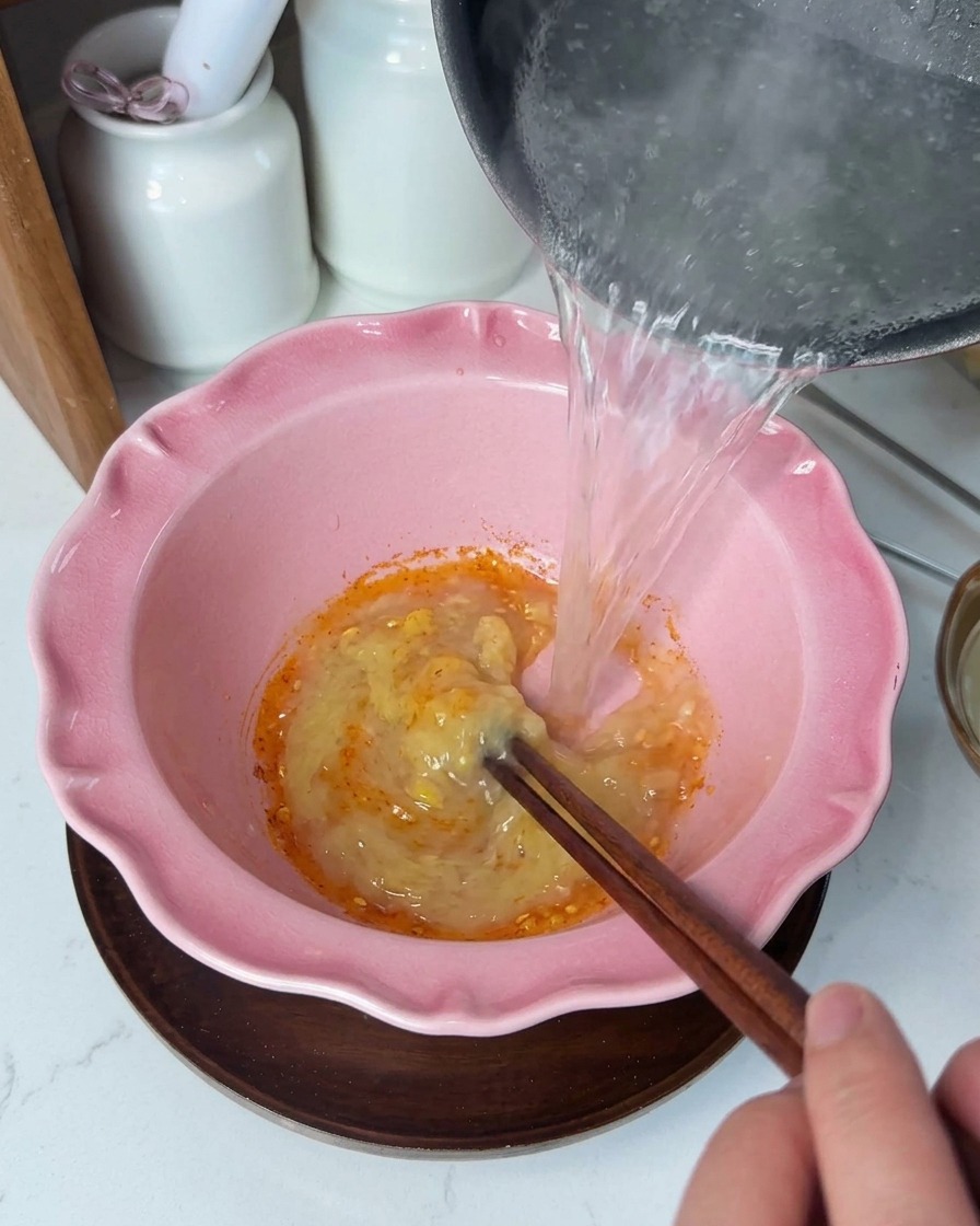 卵黄とマヨネーズの入ったどんぶりに熱々のスープを注ぎ、箸でかき混ぜる様子。