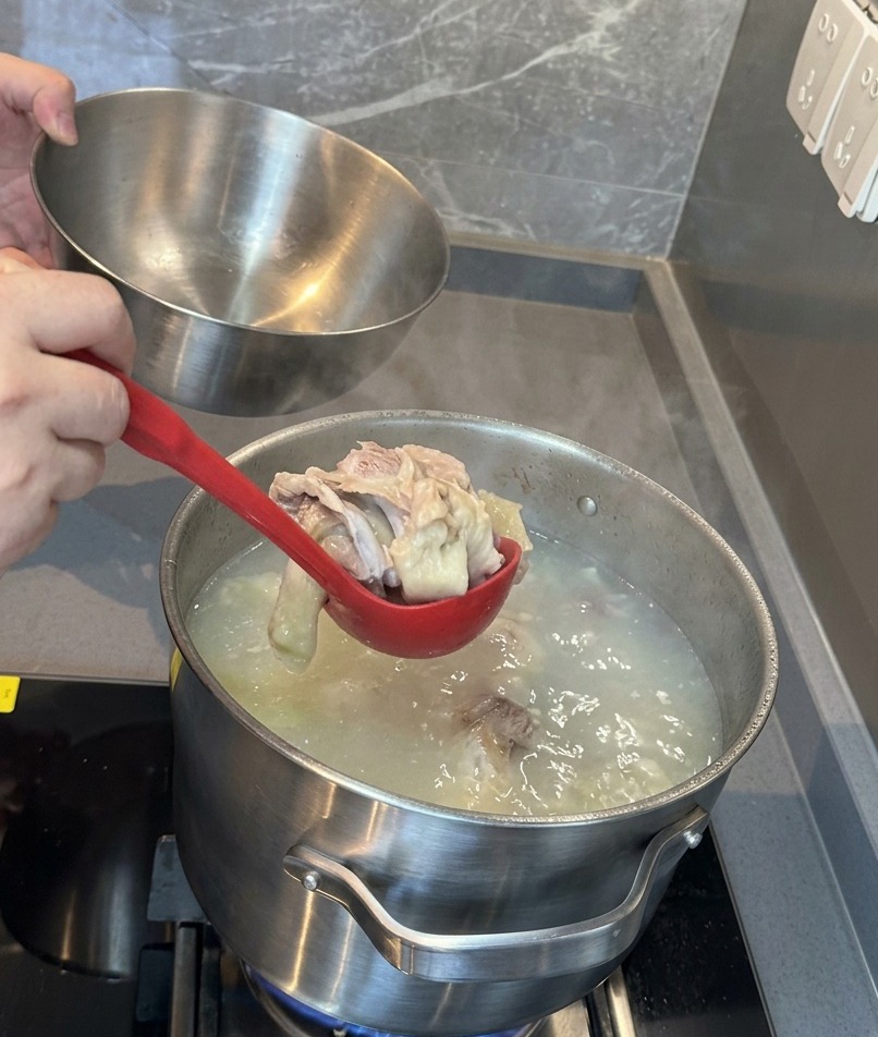 白濁したスープの中から、柔らかくなった豚肉と骨を赤いお玉でステンレスのボウルにすくい出している様子。