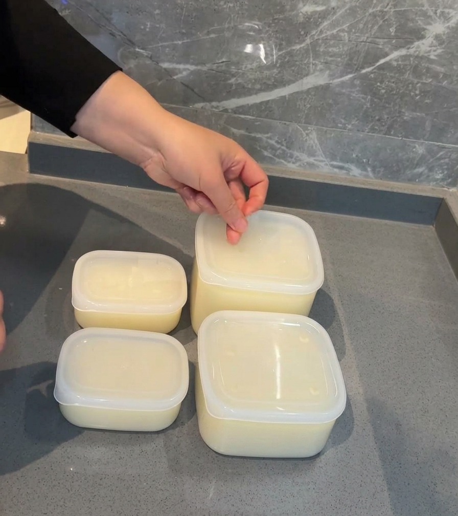 豚骨スープが入った透明なプラスチック容器の蓋に、日付を書いた白いラベルシールを貼っている手。