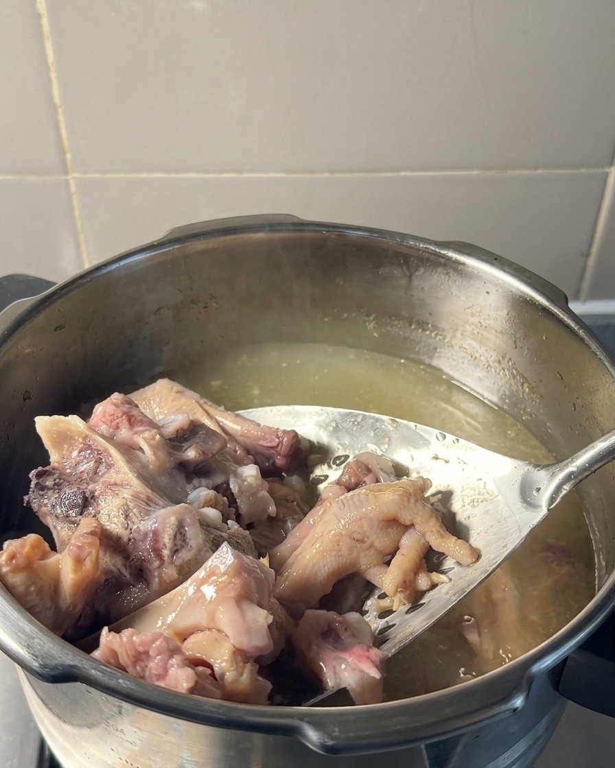穴あきターナーを使い、薄黄色いスープの入った鍋からホロホロに煮込まれた豚肉と鶏足を持ち上げている様子