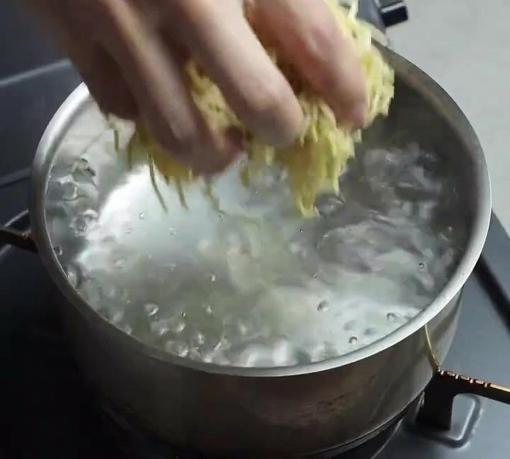 沸騰したお湯がたっぷり入ったステンレス鍋に、生の黄色い中華麺の束をそっと投入している様子。