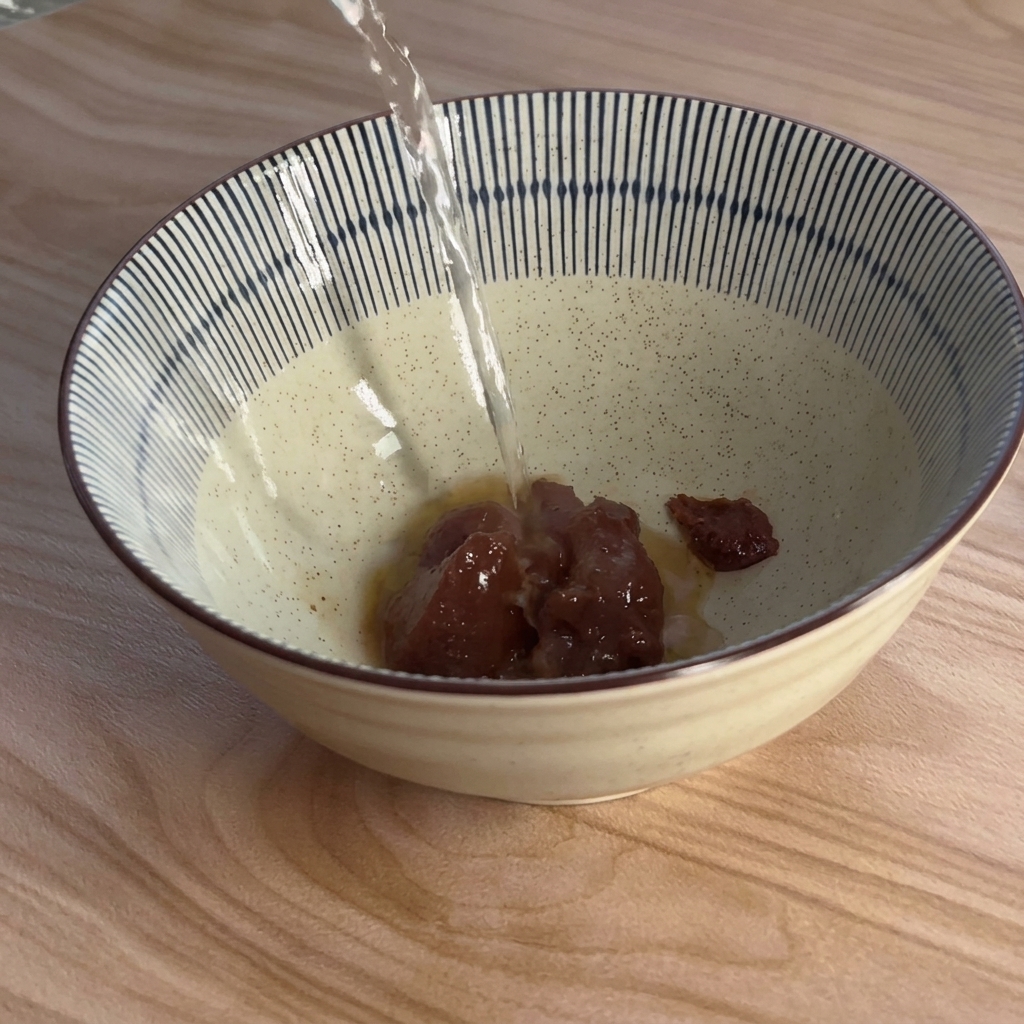 茶色い味噌ペーストが入った青と白のストライプの器に、上から熱湯を注いでいる様子。