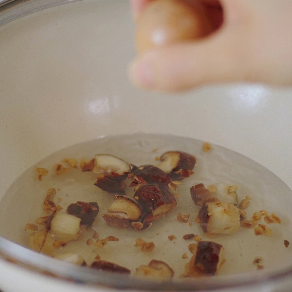 しいたけと水が入った白い鍋に、茶色い卵をそっと入れている様子