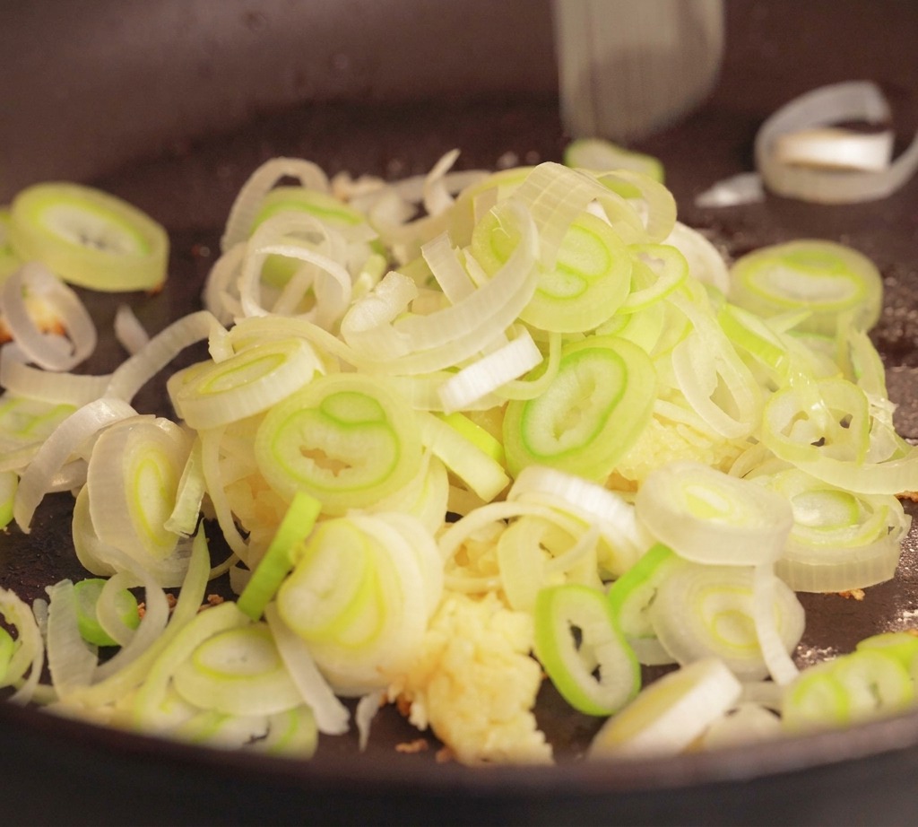 フライパンに豚ひき肉、みじん切りにしたにんにく、刻んだ青ねぎが入っている様子