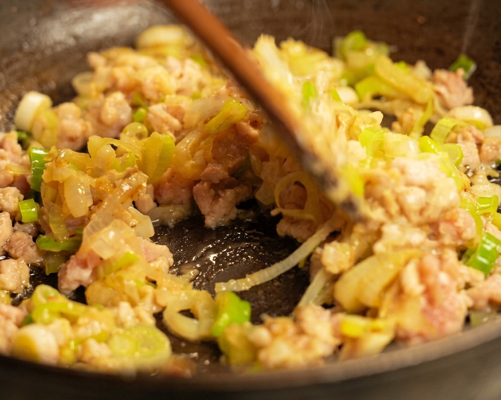 熱したフライパンで豚ひき肉と青ねぎを木べらで炒めている様子